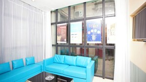 Una habitació amb un sofà blau, una taula de cafè de vidre i grans finestres amb diversos cartells.