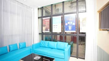 A room with a blue sofa, a glass coffee table, and large windows with various posters.