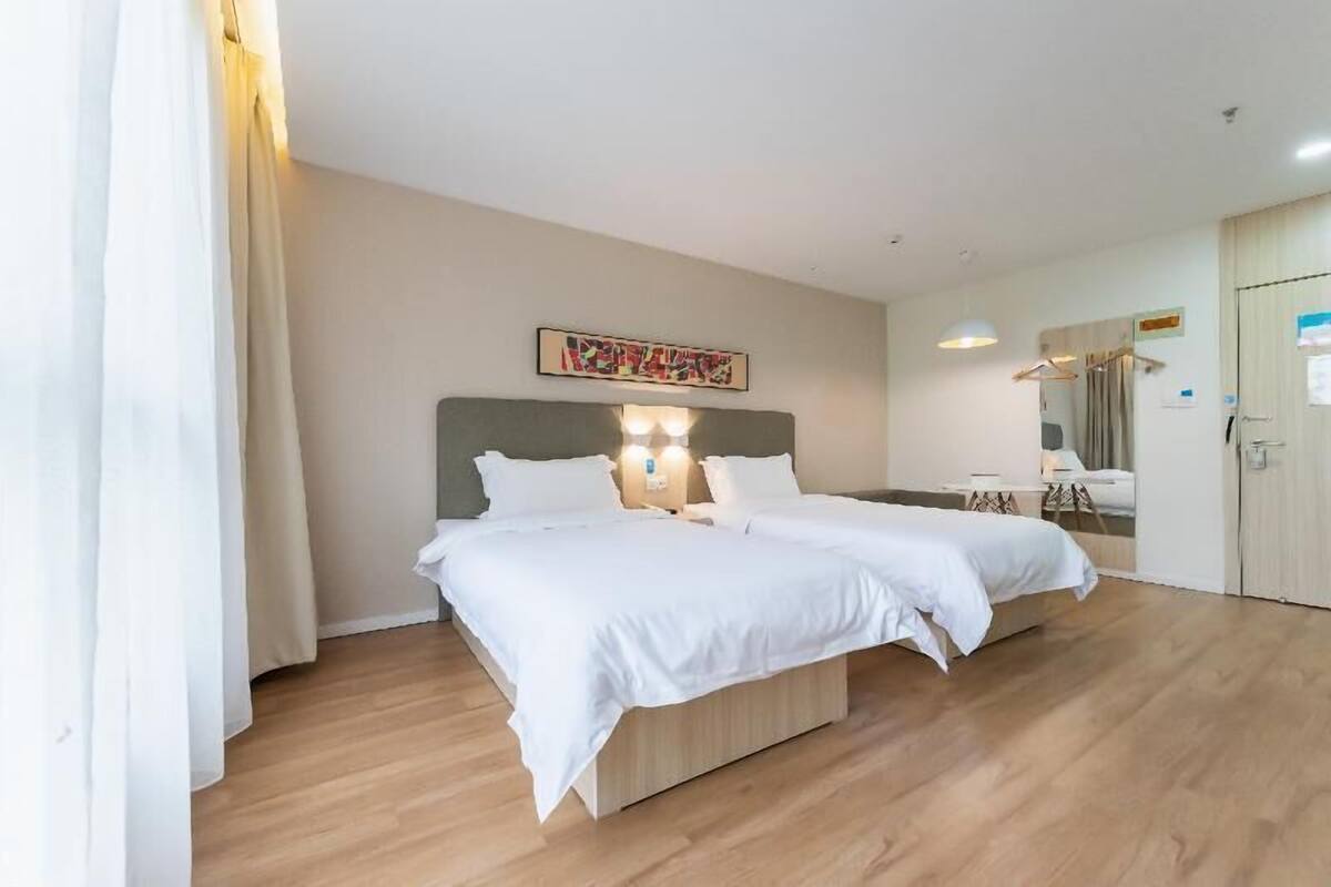A hotel room with a bed, bedside tables, a mirror, and a door.