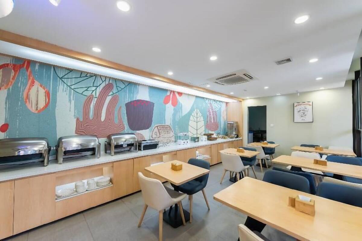 A cafeteria with a buffet line, tables, chairs, and a mural on the wall.