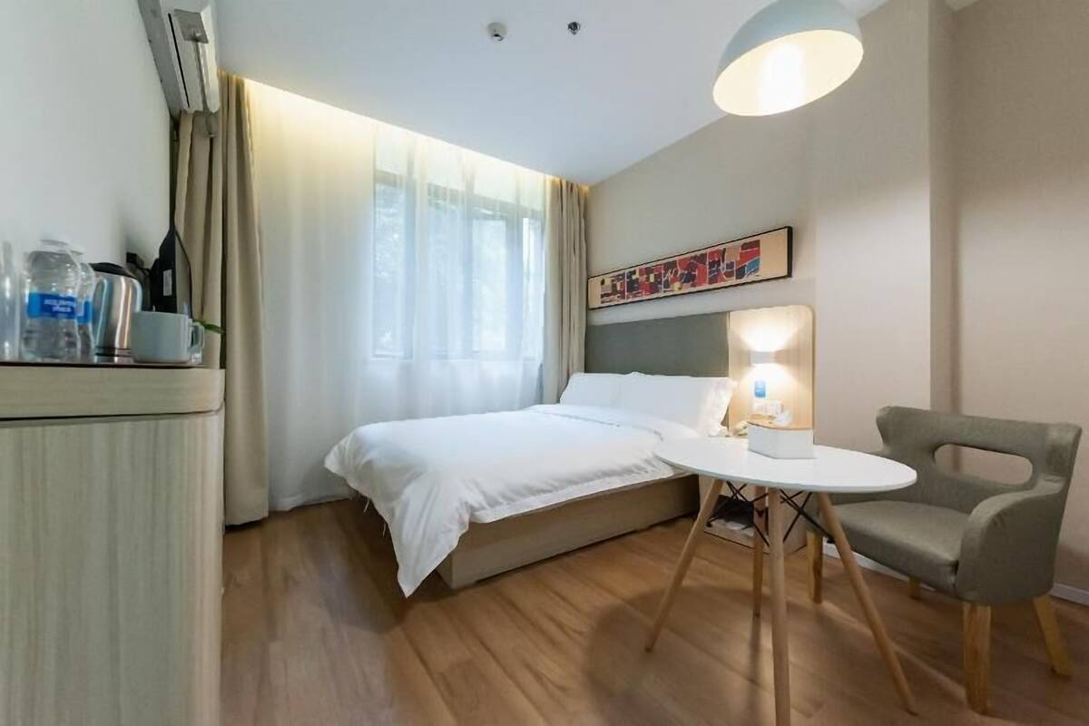 A hotel room with a bed, bedside table, chair, and a painting on the wall.