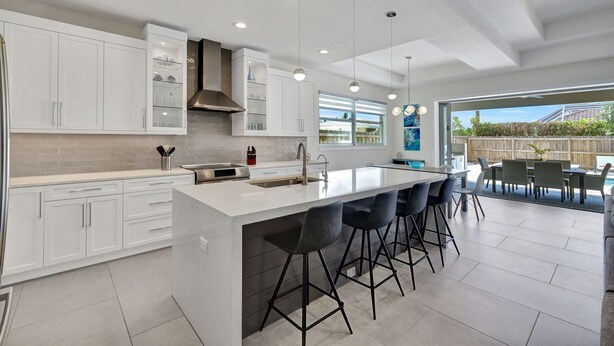 A modern kitchen with white cabinets, a large island with bar stools, and a dining area with outdoor seating. - ⭐ NEW! Starfish Wishes | Saltwater Pool & Spa • Walk to Beach • Sleeps 9 (Naples)