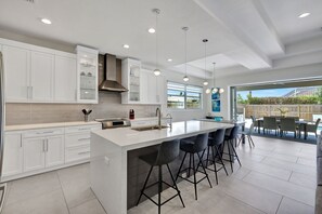 A modern kitchen with white cabinets, a large island with bar stools, and a dining area with outdoor seating.
