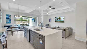 A modern kitchen with a central island, built-in appliances, and a dining area with a view to the outdoors. - ⭐ NEW! Starfish Wishes | Saltwater Pool & Spa • Walk to Beach • Sleeps 9 (Naples)