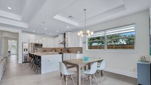 A modern kitchen with a central island, bar stools, and a dining table with chairs. - ⭐ NEW! Starfish Wishes | Saltwater Pool & Spa • Walk to Beach • Sleeps 9 (Naples)