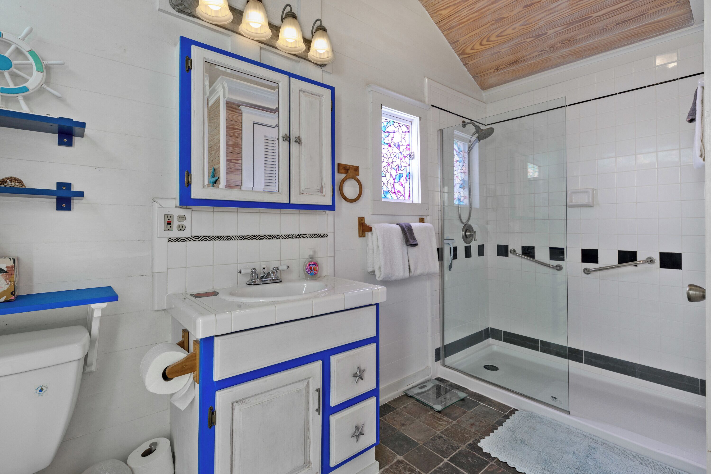 Ein Badezimmer mit einem weißen Waschbecken, blauen Schränken, einer Duschkabine aus Glas und einer Holzbeschichtung an der Decke.