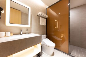 Un baño moderno con cabina de ducha de vidrio, un inodoro blanco y un tocador con espejo.