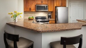A kitchen with wooden cabinets, a stainless steel refrigerator, a microwave, a stove, and a coffee maker. There are two chairs and a vase with flowers on the counter. - 2 BD/2BA Full Size Villa @ Marriot's Shadow Ridge I - The Villages - BNP Tennis! (Palm Desert)