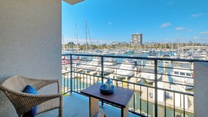 A balcony with wicker furniture and a small table, overlooking a marina with various boats and a distant building.