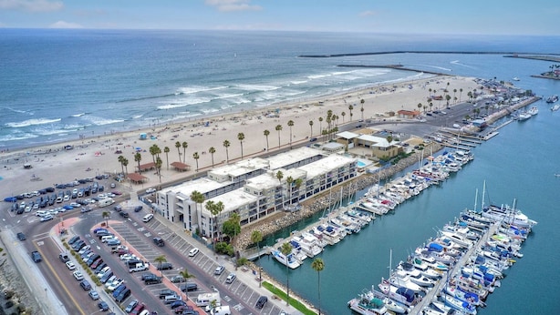 An aerial view of a coastal area with a marina, beach, and adjacent buildings.