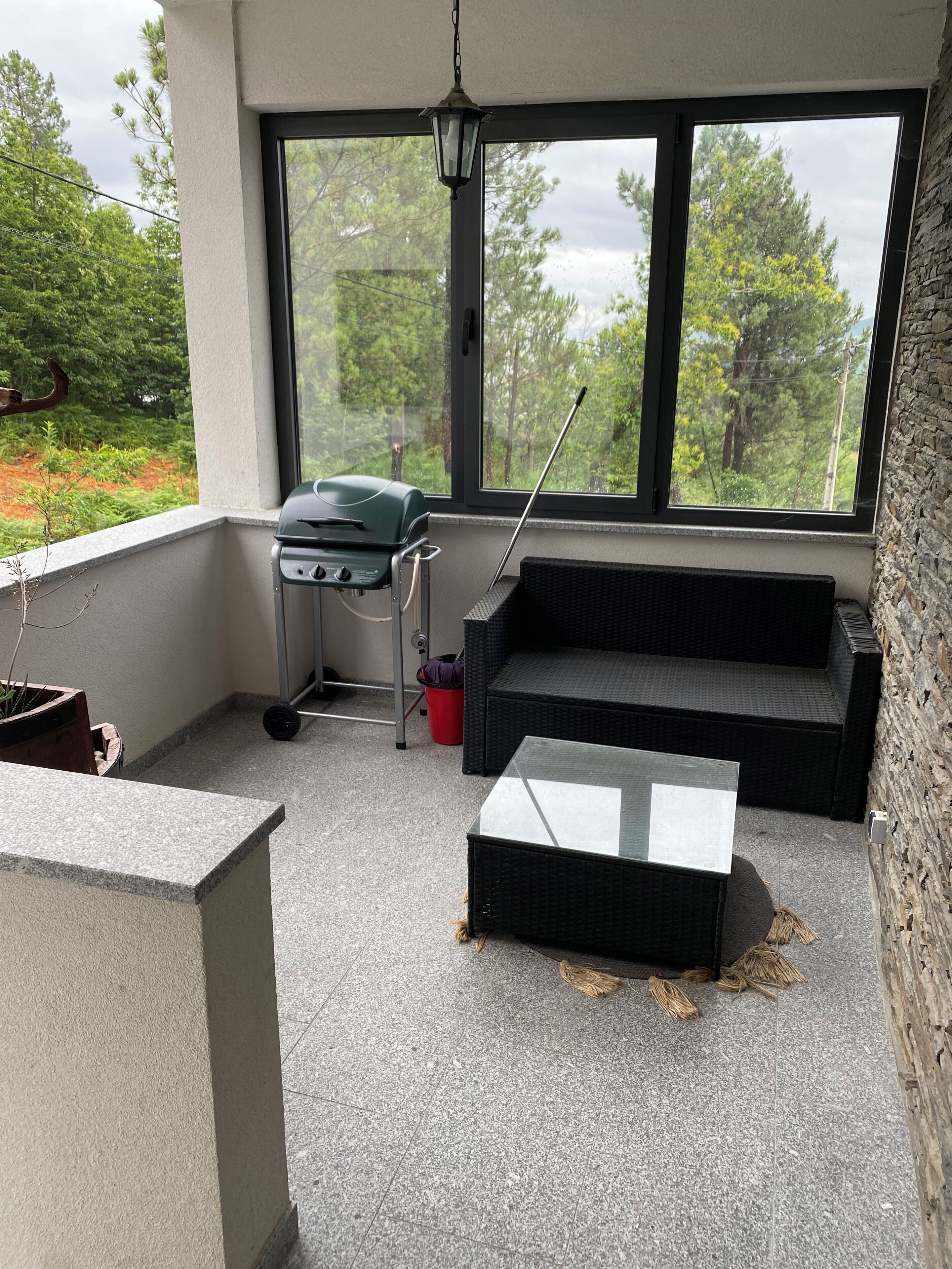 A balcony with a grill, a wicker sofa, and a glass table.