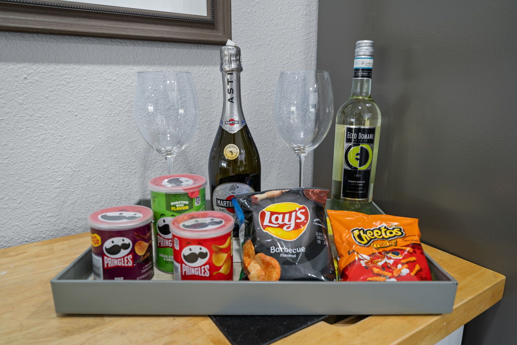 A tray with snacks, drinks, and two glasses on a wooden table.