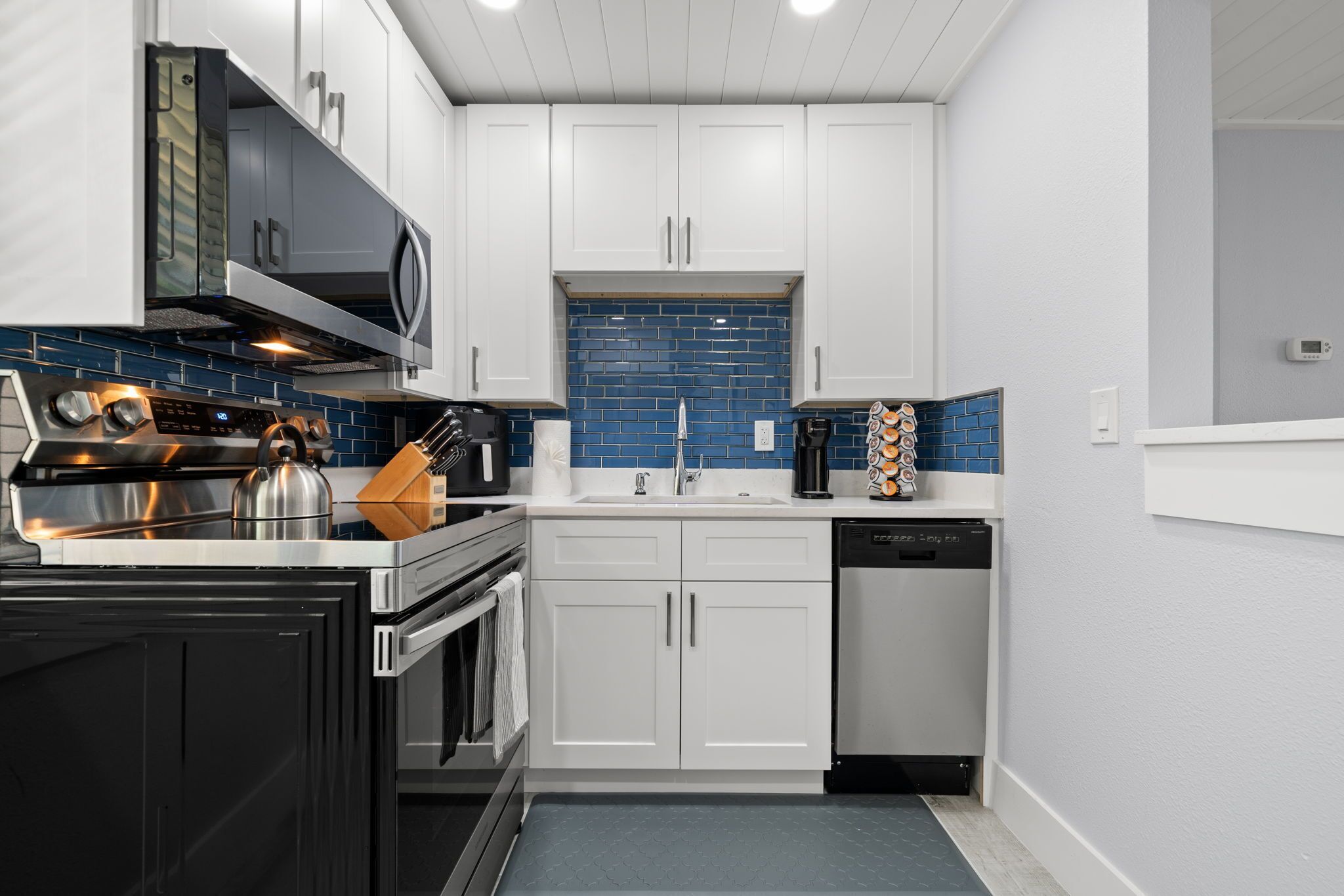 Una cucina moderna con pensili bianchi, una cappa in acciaio inossidabile, un backsplash in piastrelle blu e una lavastoviglie.