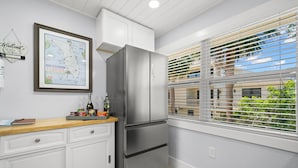 Una cocina con refrigerador de acero inoxidable, armarios blancos, un mapa enmarcado en la pared y una ventana con persianas.