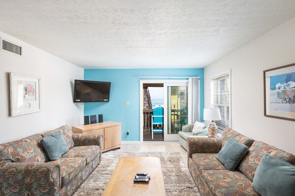 Bright coastal living room with comfortable seating, smart TV, and direct access to the ocean-view balcony. - Oceanfront 2BR/2BA Condo | Pet Friendly | Kill Devil Hills OBX (Kill Devil Hills)