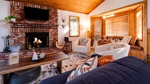 A cozy living room with a brick fireplace, wooden ceiling, and comfortable seating. - Hot tub, bbq, 2 fireplaces, 5 mins to slopes & lake (Big Bear Lake)