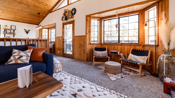 A cozy cabin interior with a wooden ceiling, large windows, a sofa, a chair, and a coffee table. - Hot tub, bbq, 2 fireplaces, 5 mins to slopes & lake (Big Bear Lake)
