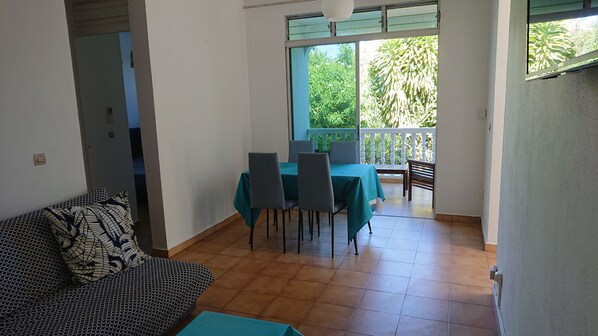 Ein Zimmer mit einer Couch, einem Esstisch mit Stühlen und einem Balkon mit Geländer.