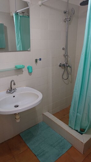Ein Badezimmer mit Waschbecken, Spiegel, Dusche und einem türkisfarbenen Duschvorhang.