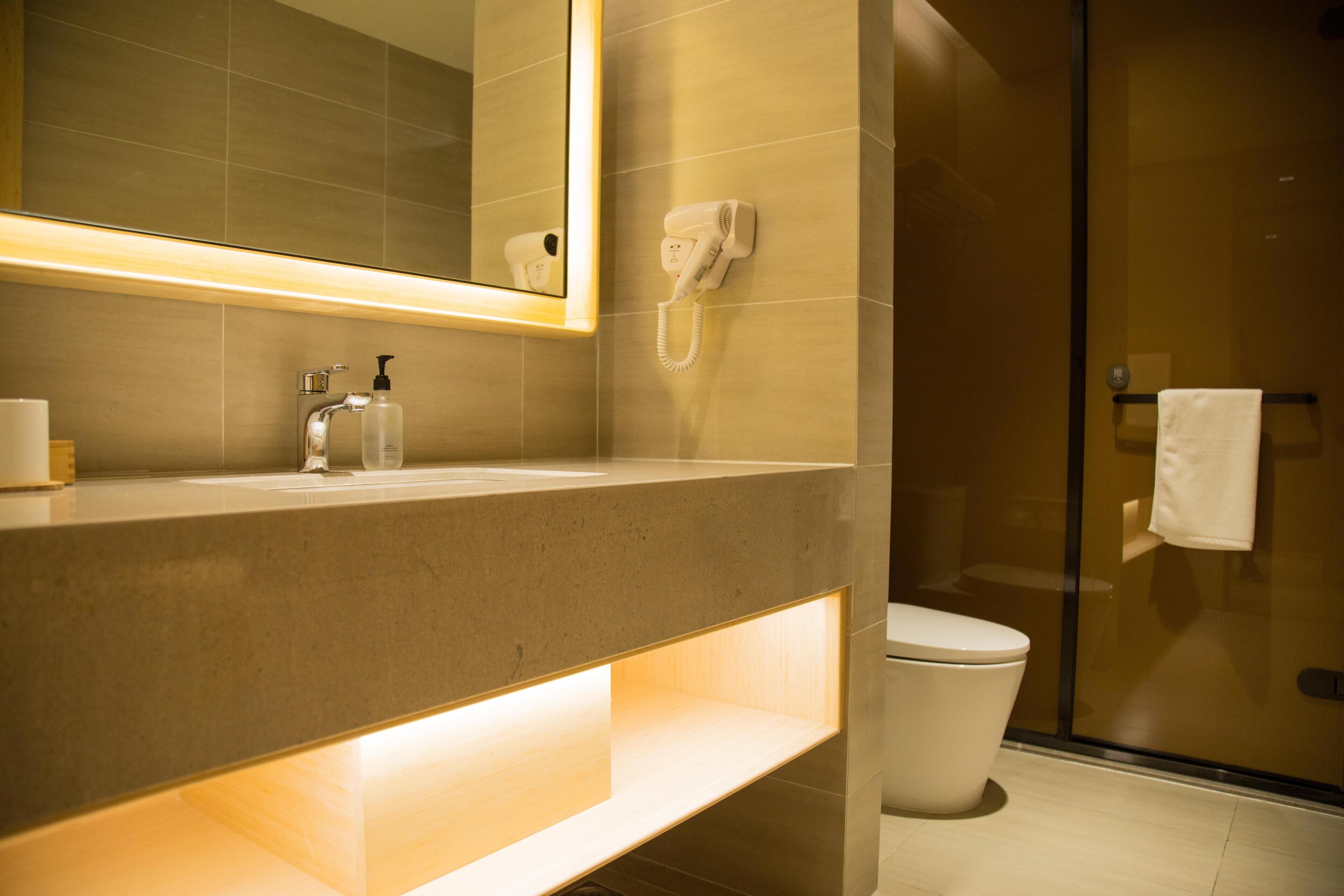 Une salle de bain moderne avec un meuble-lavabo, un sèche-cheveux fixé au mur et une cabine de douche en verre.