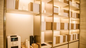 Una habitación bien iluminada con estanterías de madera llenas de libros y objetos decorativos. Hay una cafetera, un hervidor y una bandeja con tazas y una caja sobre la encimera.