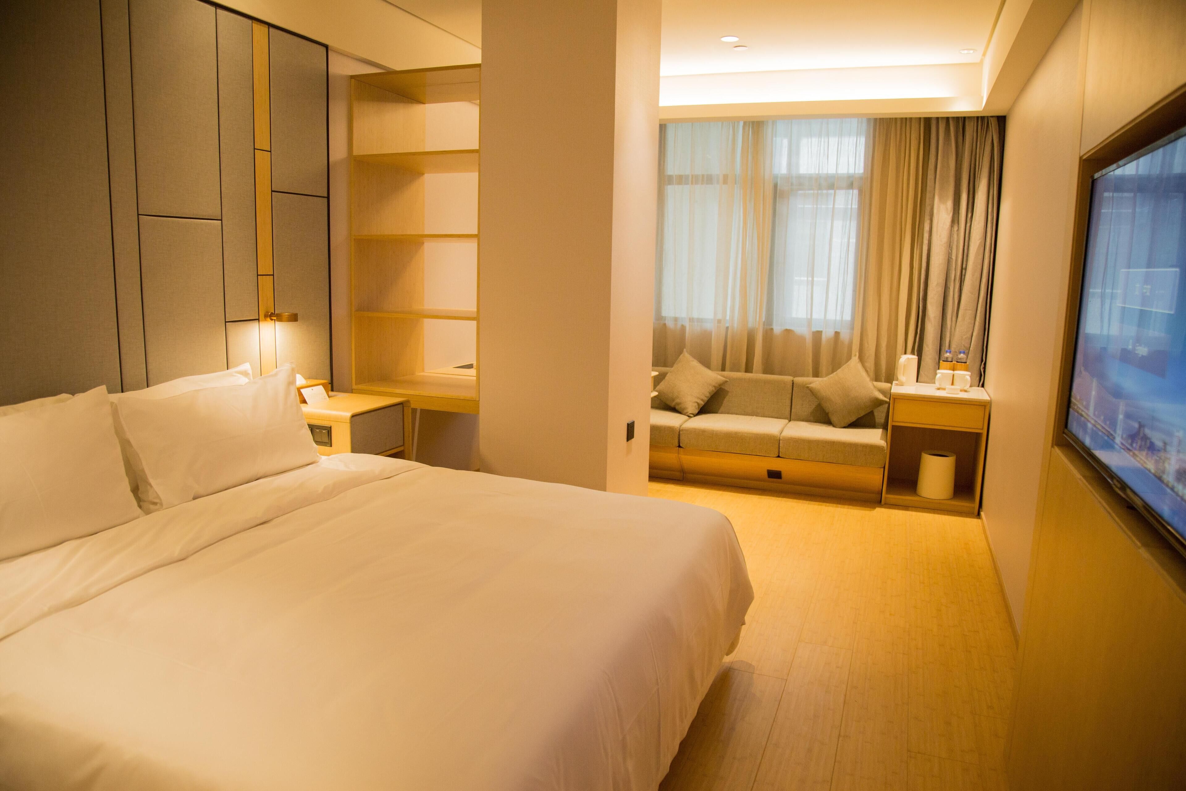 Une chambre d’hôtel avec un grand lit, un coin salon avec un canapé et des rideaux, une télévision et une bibliothèque.