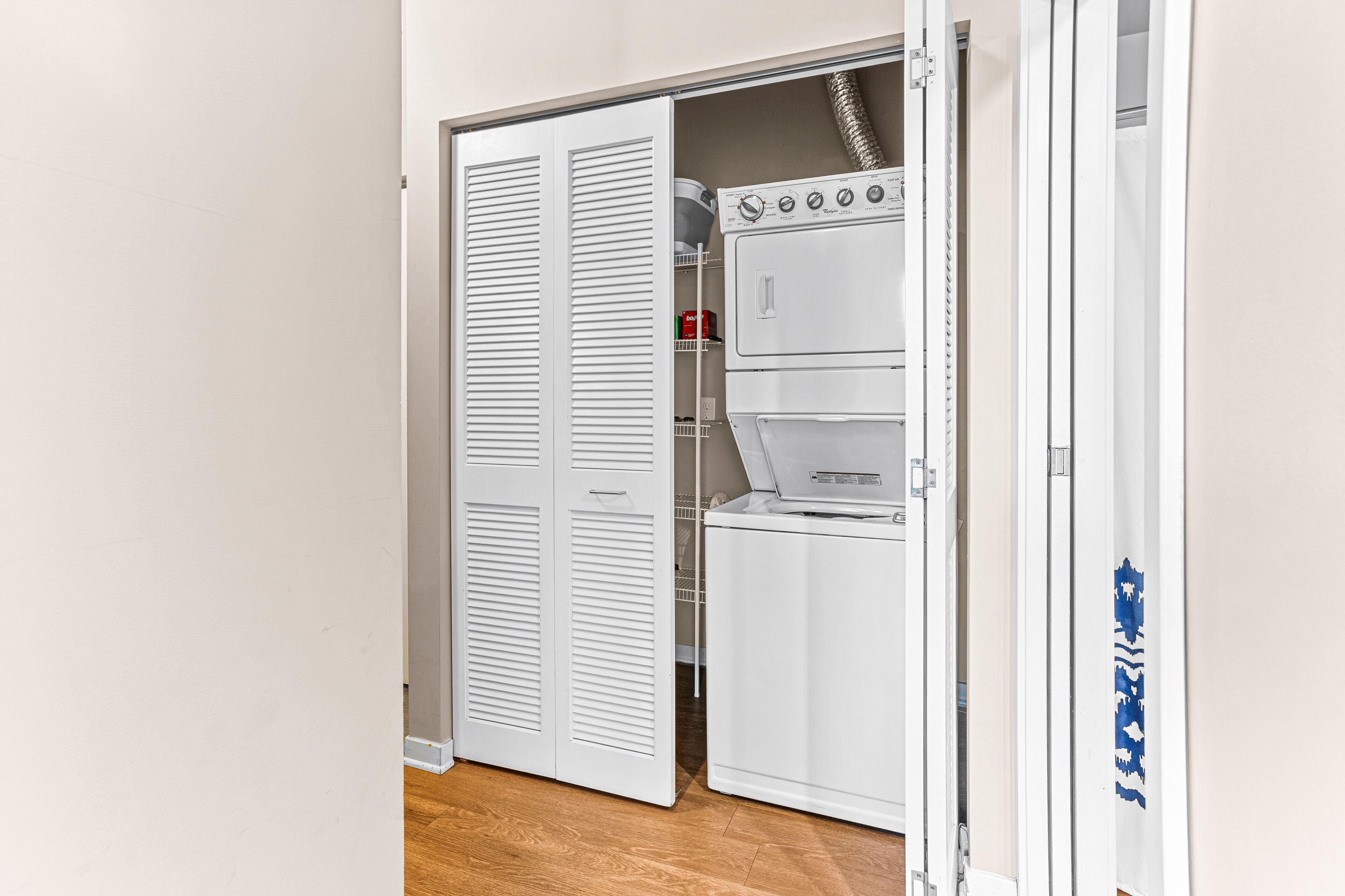 A laundry room with a stacked washer and dryer, a white closet with louvered doors, and a metal shelving unit.