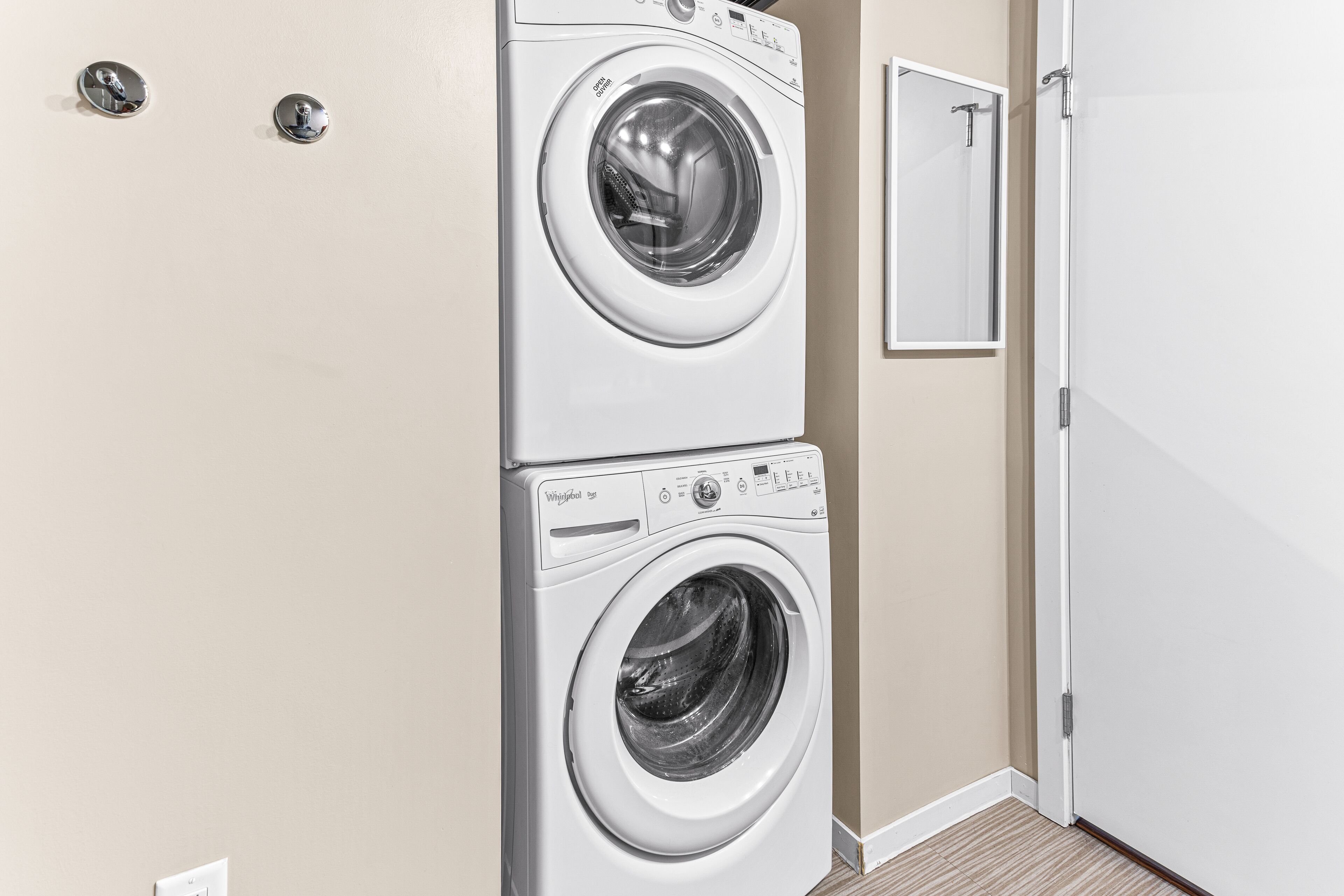 A laundry room with two stacked front-loading washing machines and a mirror on the wall.