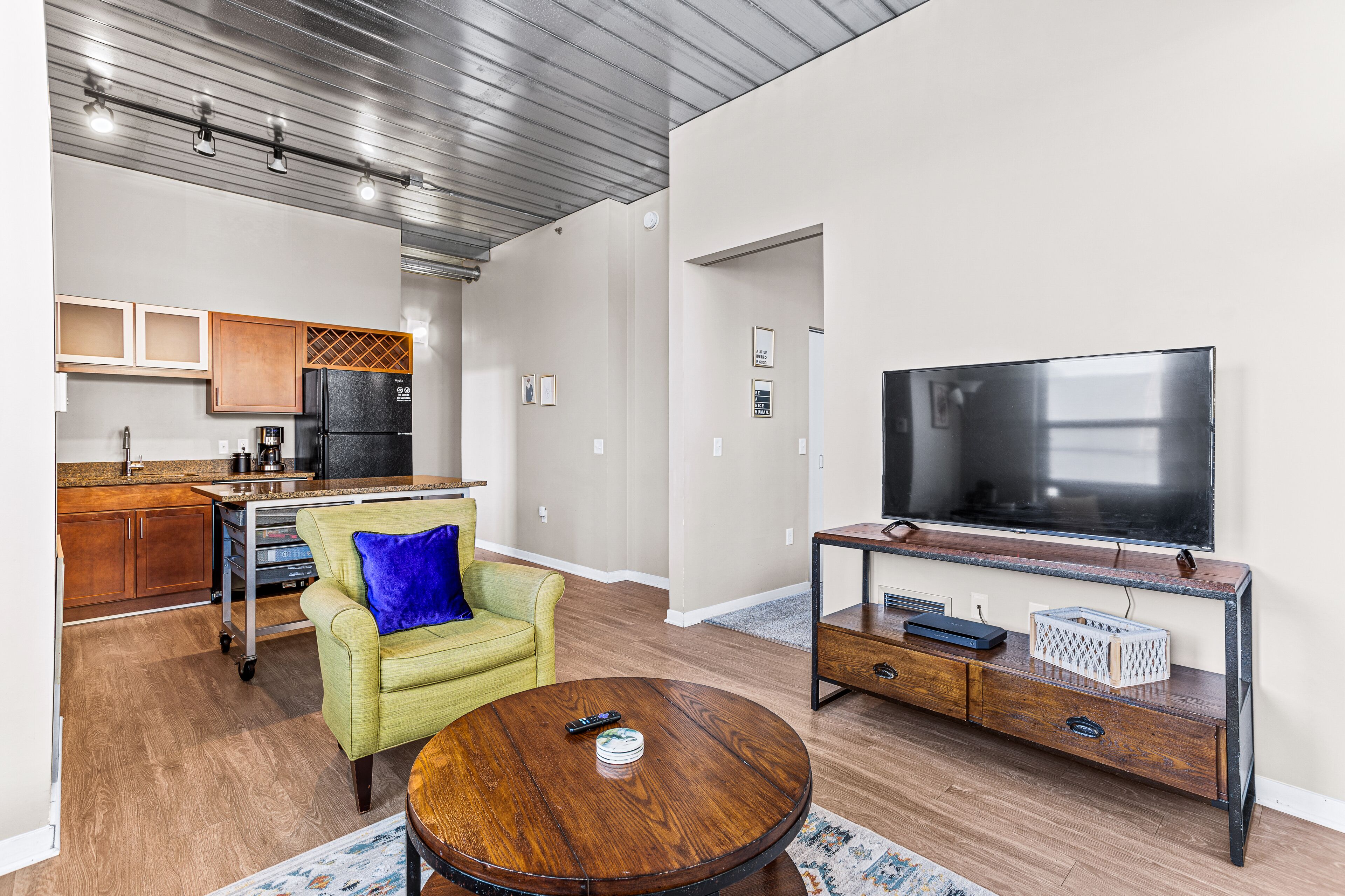 Una sala de estar moderna con una mesa de centro de madera, un sillón verde y un televisor sobre un mueble de madera.