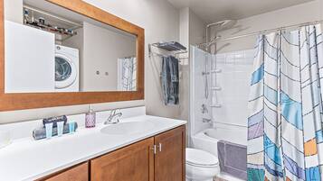 Un baño moderno con lavadora integrada, lavamanos dobles y ducha con cortina estampada.