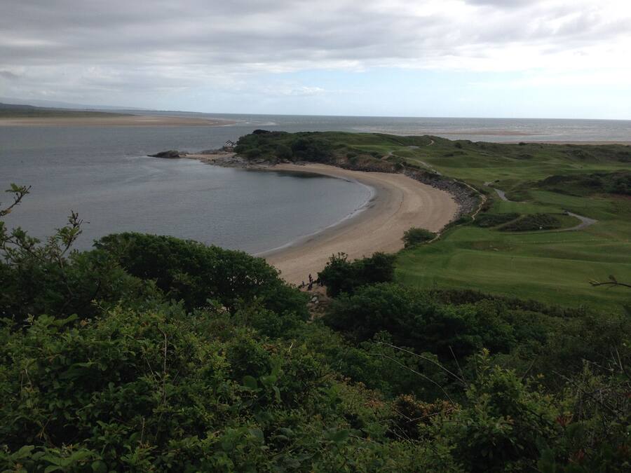 A coastal landscape with a sandy beach, a golf course, and a body of water.