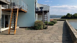 A waterfront property with a balcony, a wooden ladder, and a stone pathway leading to a canal. - 48A South Snowdon Wharf (Porthmadog)