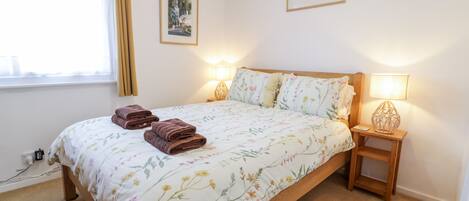 Una cama bien hecha con ropa de cama floral, dos lámparas de noche y un ventanal con cortinas.