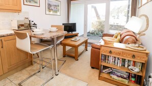 A modern kitchen with a dining area, a television, and a bookshelf with books. - 48A South Snowdon Wharf (Porthmadog)