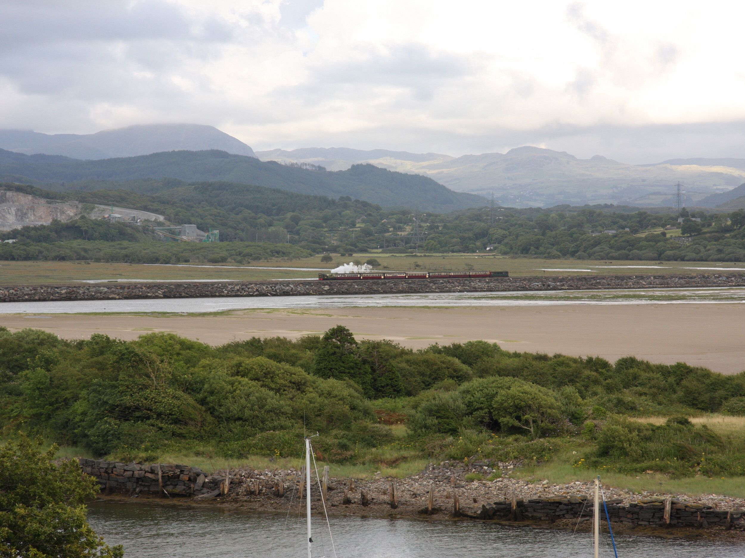 A scenic landscape with a river, a stone wall, and distant mountains.