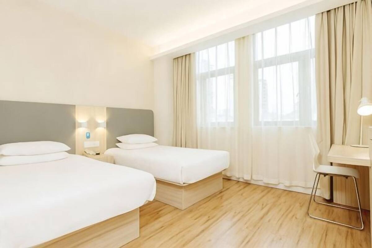 A hotel room with two beds, a desk, and a window with curtains.