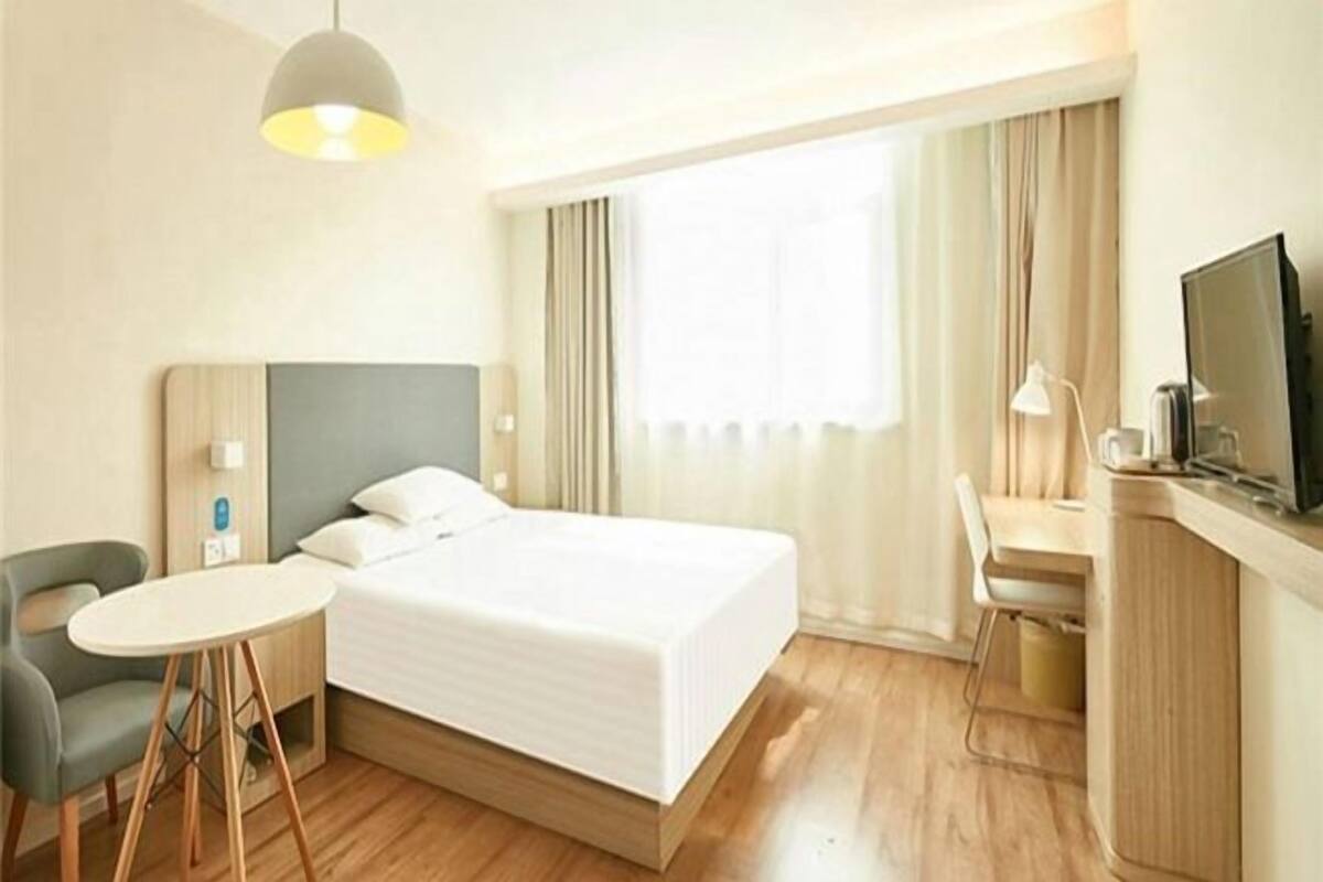A hotel room with a bed, a desk, a chair, a TV, and a window with curtains.