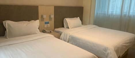 A hotel room with two single beds, a bedside table with a phone, and a window with sheer curtains.
