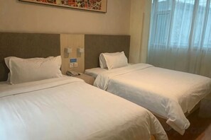 Quarto de hotel com duas camas de solteiro, mesa de cabeceira com telefone e janela com cortinas finas.