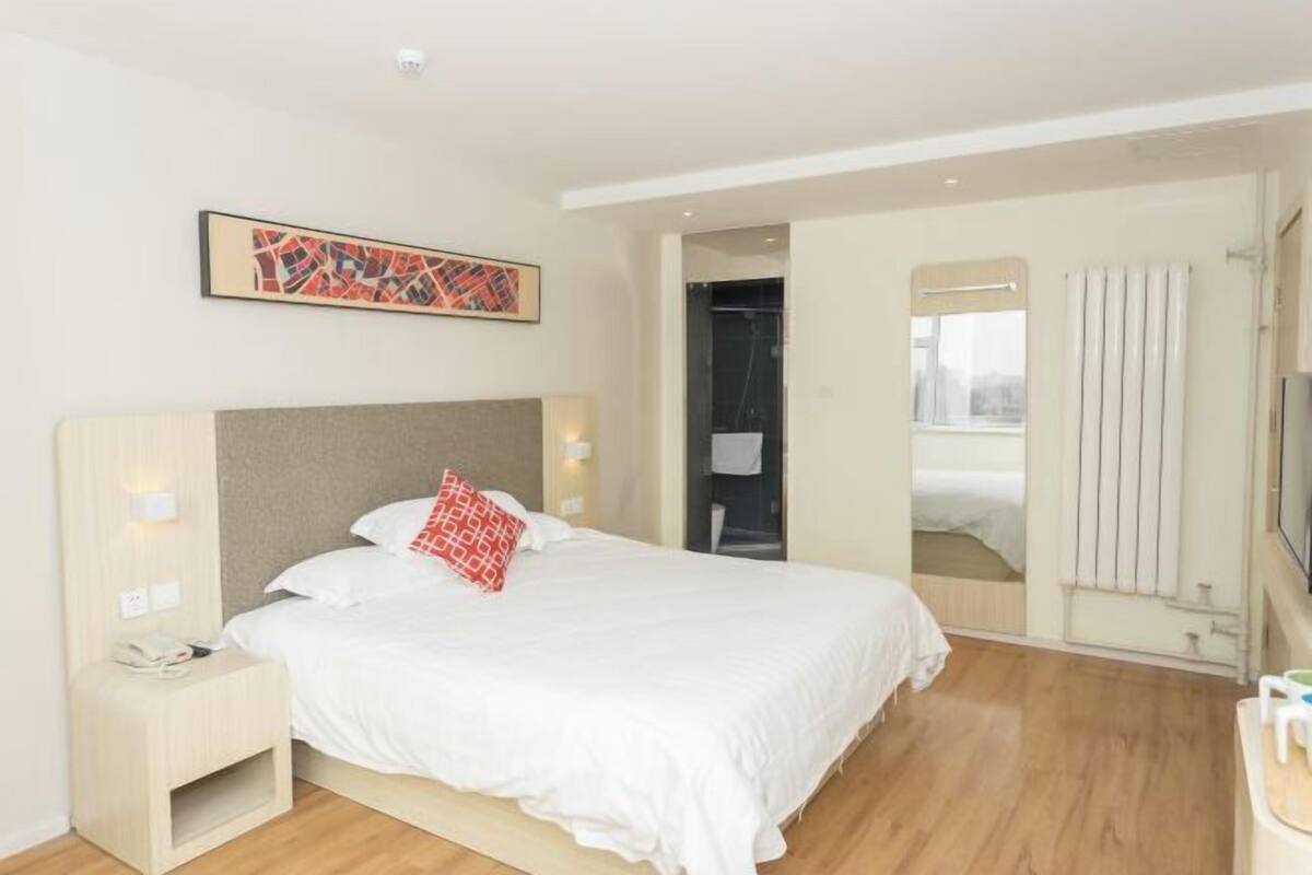 A hotel room with a bed, bedside table, artwork, and a view through an open door.