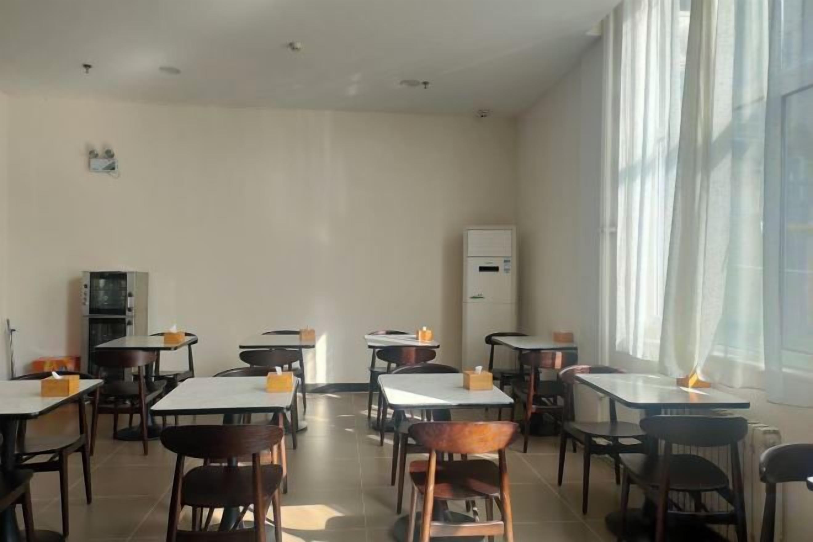 A dining area with tables and chairs, a refrigerator, and a window with curtains.