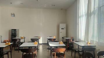 A dining area with tables and chairs, a refrigerator, and a window with curtains.
