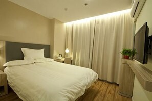 Une chambre d’hôtel comprenant un lit, une table de chevet, une lampe, des rideaux et un téléviseur.