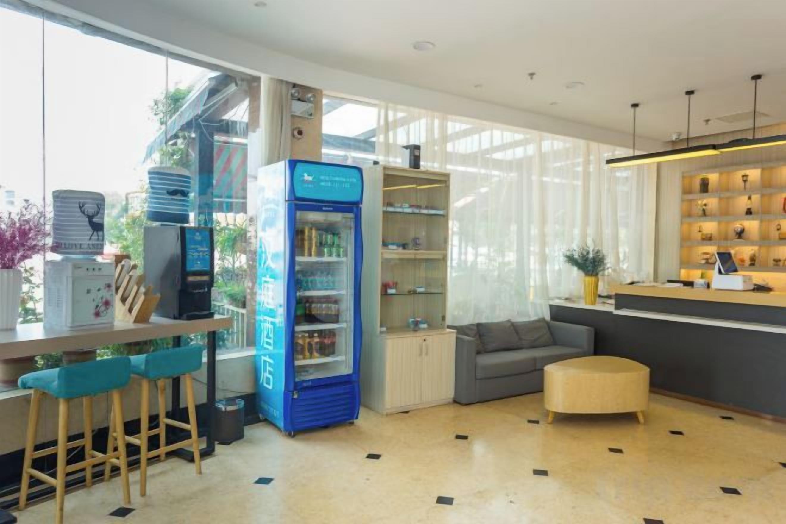 A modern hotel lobby with a seating area, a blue minibar, and a reception desk.