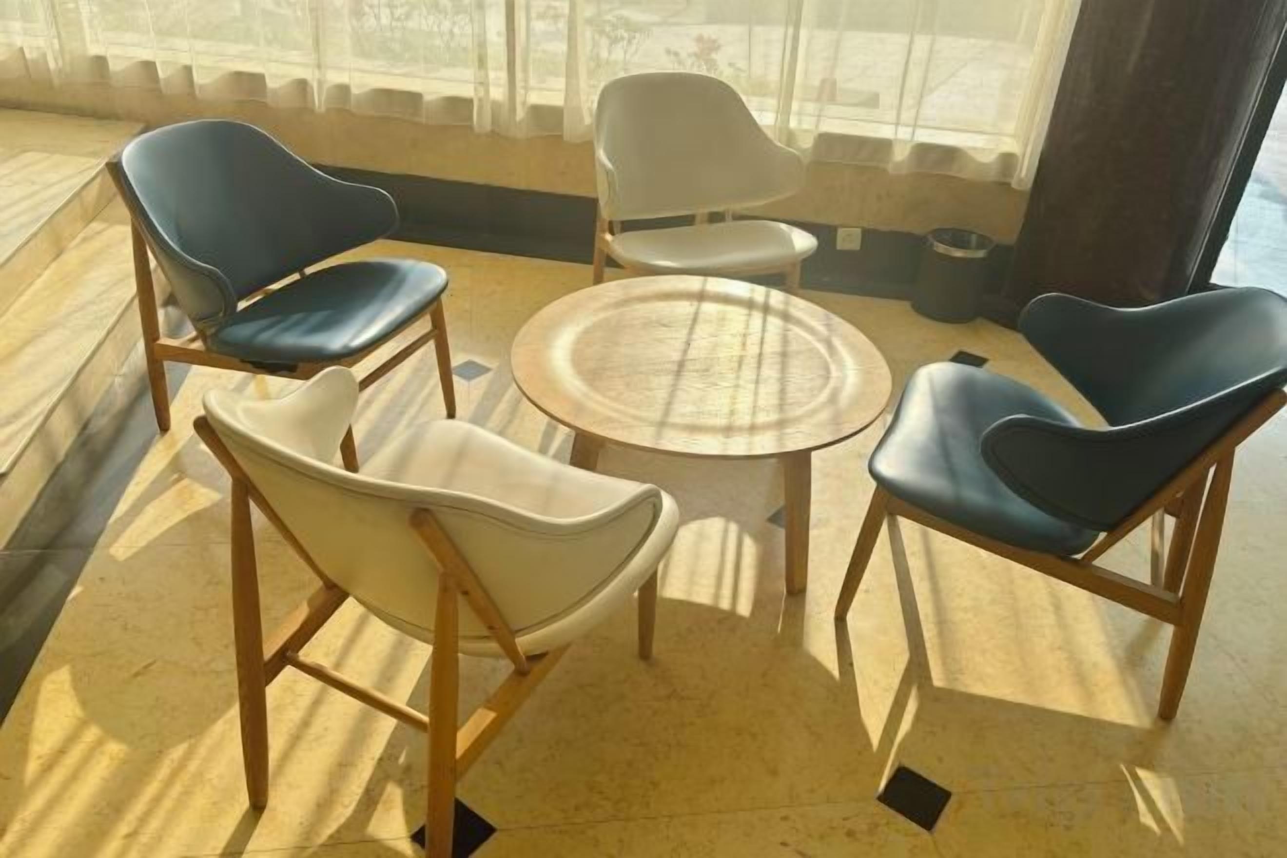 A seating area with four chairs and a round table, arranged on a tiled floor with a view through large windows.