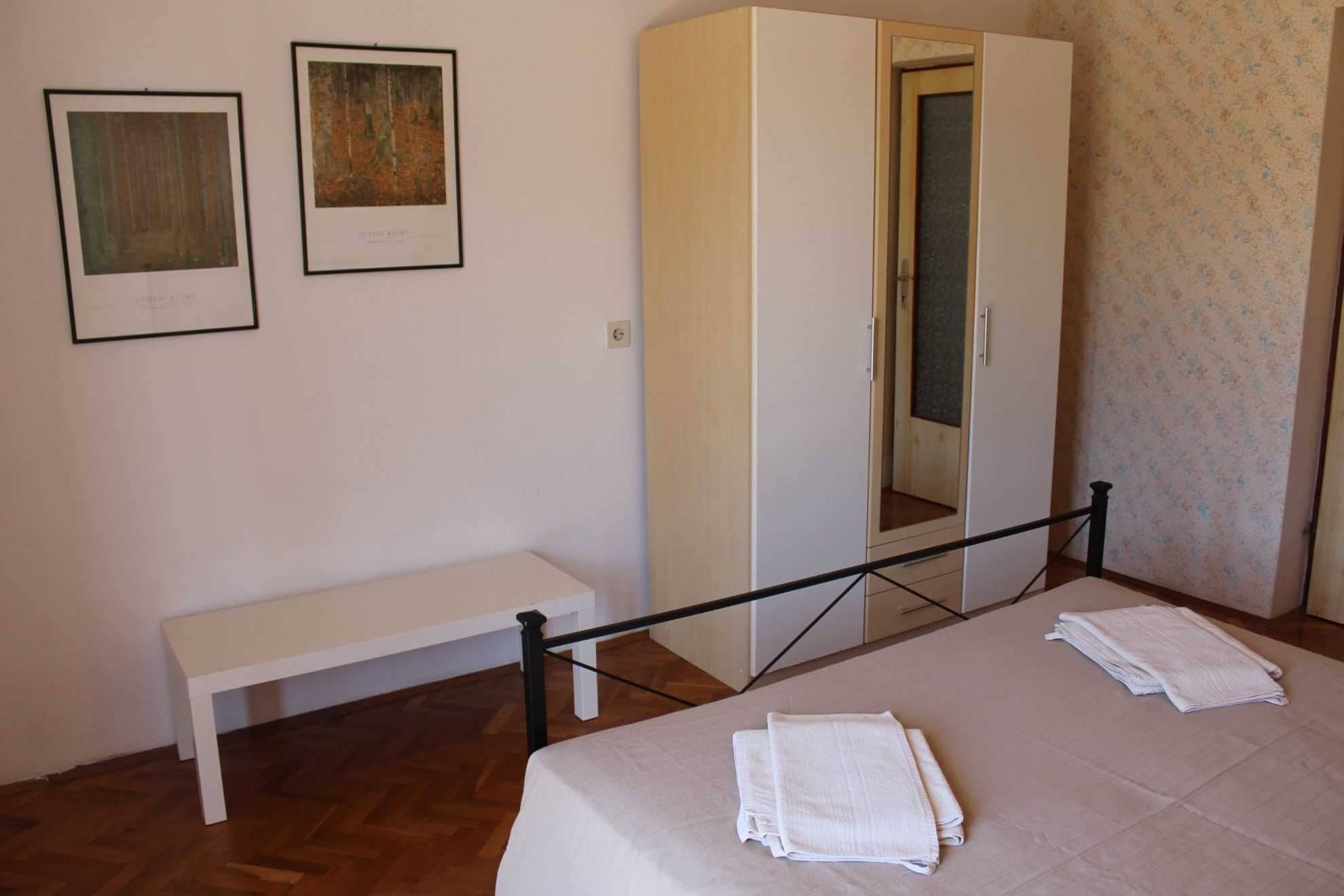 Une chambre à coucher comprenant un lit, un banc, une armoire et deux tableaux encadrés accrochés au mur.