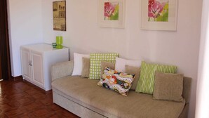 A living room with a beige sofa, patterned cushions, a white cabinet, and framed floral artwork on the wall. - Apartment Casa Monte Mulini 1/1 (Rovinj)