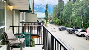 A balcony with outdoor seating, a view of a mountain range, and parked vehicles. - The overlook stay - Free parking - 26 (Harvie Heights)