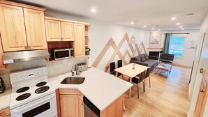 A modern kitchen with wooden cabinets, a built-in microwave, and a stove. There is a dining area with a table and chairs, and a sofa. - The overlook stay - Free parking - 26 (Harvie Heights)