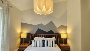 A bedroom with a bed, two bedside tables, a wall-mounted lamp, and a mountain mural. - The overlook stay - Free parking - 26 (Harvie Heights)